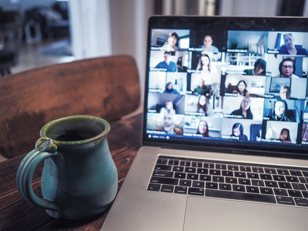 a laptop with a zoom call, with a cup next to it